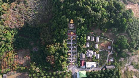 aerial drone of a unique temple with a golden buddha on a mountain surrounded by coconut trees in ao nang krabi thailand