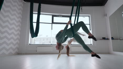 una joven hermosa mujer realiza ejercicios en una hamaca de aero yoga. una mujer por la tarde frente al espejo en la sala realiza estiramientos sola