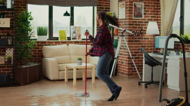 Glad kvinde danser i stuen og bruger moppen til at rengøre gulve