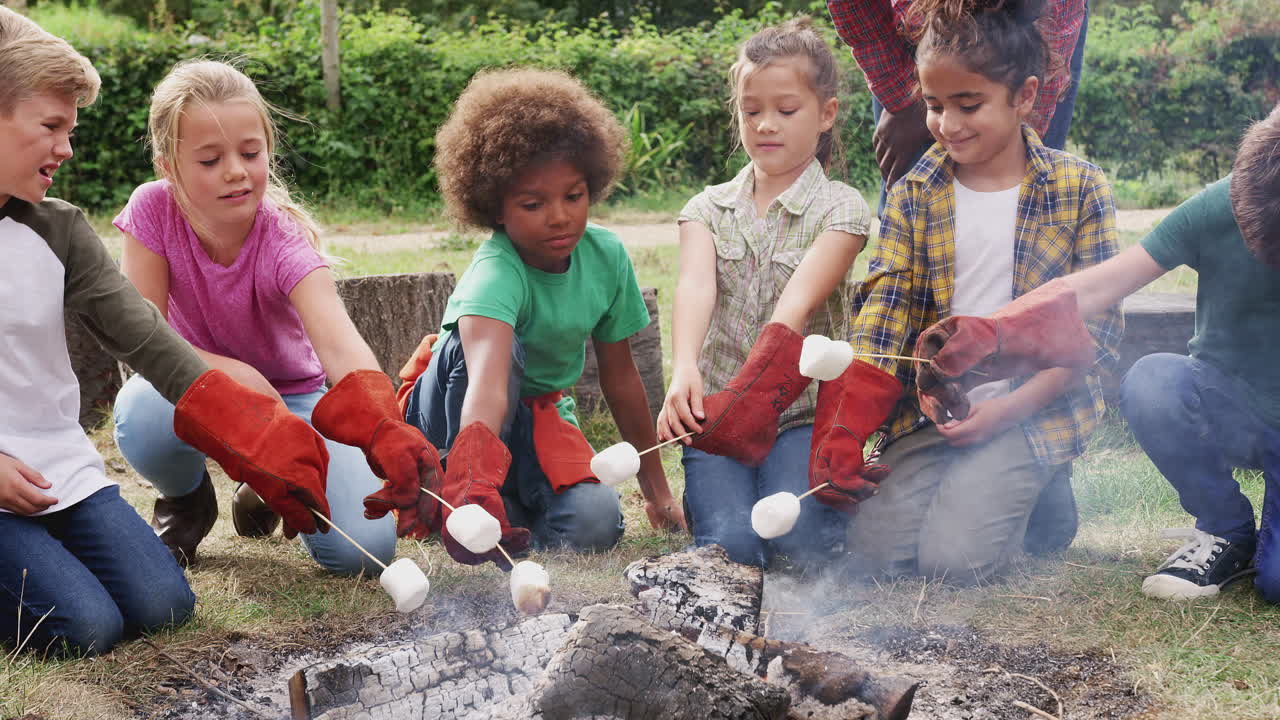 líder del equipo con un grupo de niños en un viaje de actividad al aire libre brindando malvaviscos sobre el fuego del campamento