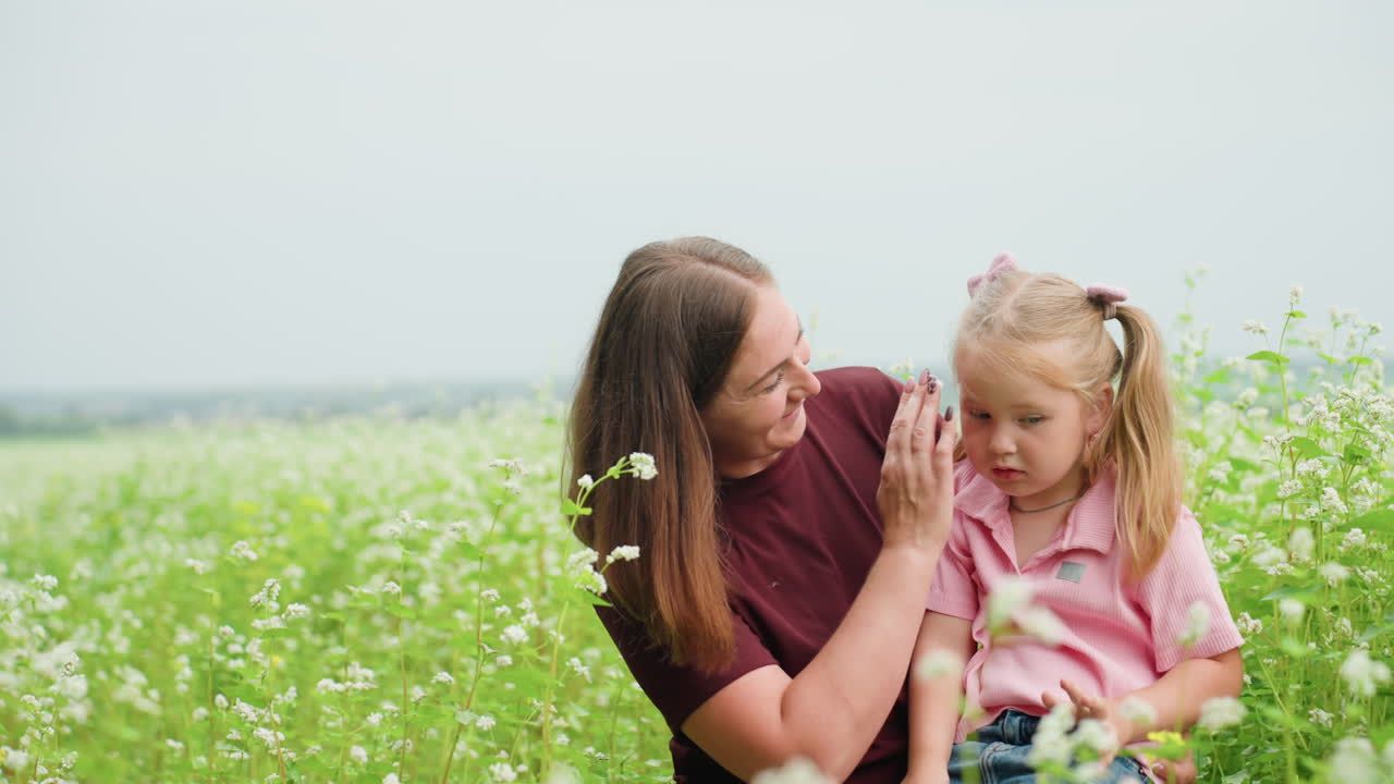 Mutter und Tochter erkunden ein Blumenfeld, verspielte Entdeckung und Lachen, zeigen auf Blüten, Kind kichert, natürliche Kulisse, Freizeitkleidung, weinrotes Oberteil und rosa Kleid, offener Lernmoment