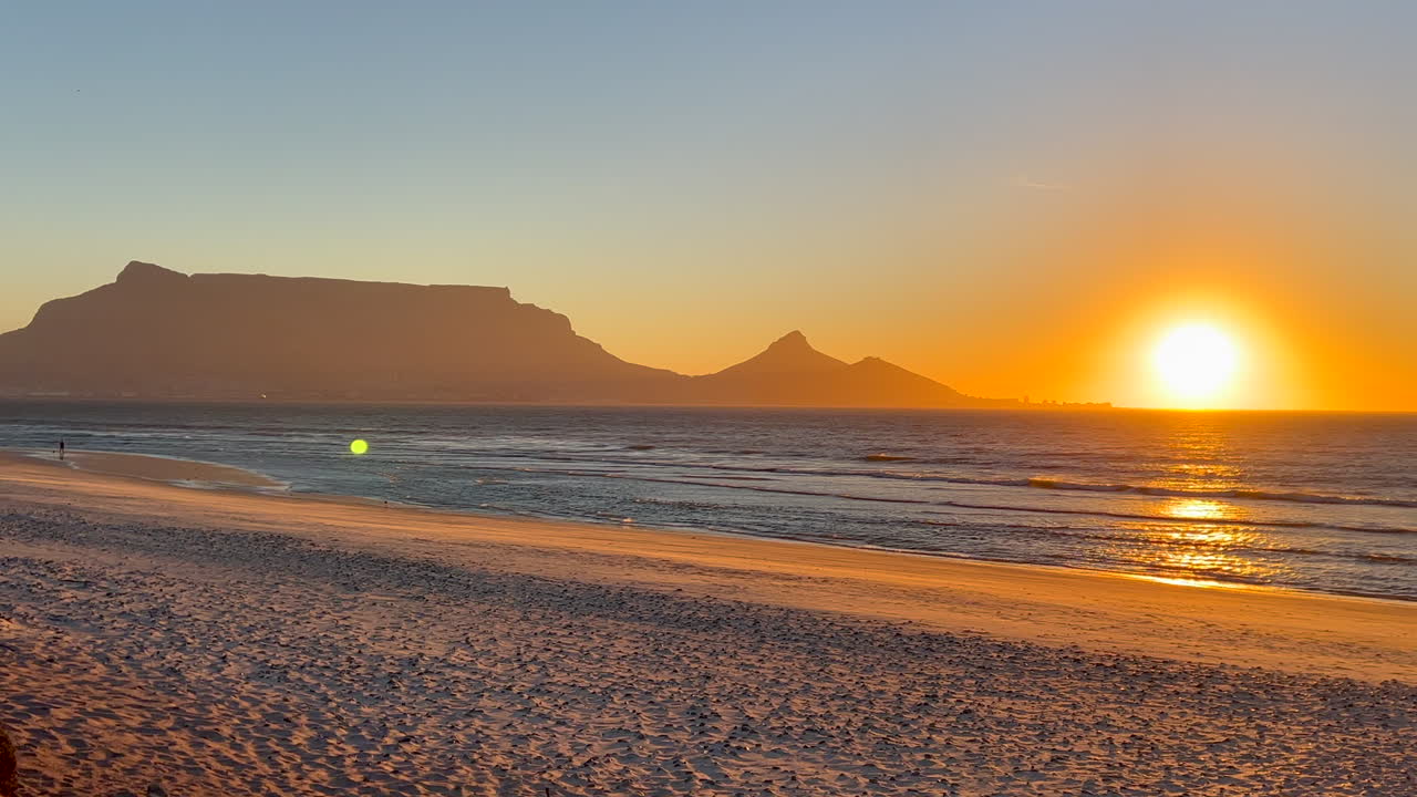 Golden sunset sun on horizon glare artifact stunning Cape Town Table Mountain Lions Head beach landscape South Africa low tide man fishing slow motion pan to the right