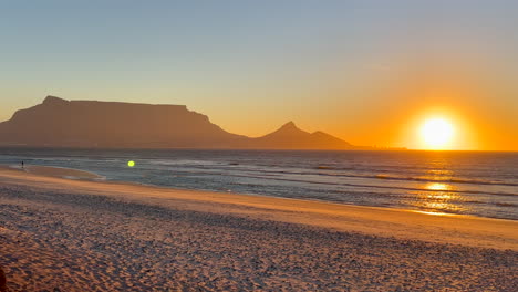 Goldener-Sonnenuntergang,-Sonne-Am-Horizont,-Blendung,-Artefakt,-Atemberaubender-Tafelberg-Von-Kapstadt,-Löwenkopf,-Strandlandschaft,-Südafrika,-Ebbe,-Mann-Beim-Angeln,-Zeitlupe,-Schwenk-Nach-Rechts