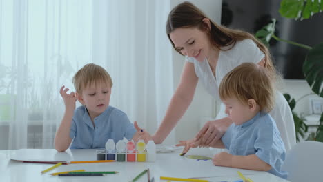 Mom-helps-her-sons-to-develop-creative-skills-and-is-engaged-with-them-to-create-drawing-paints-with-the-help-of-fingers.-Child-development.-Creative-family.-Loving-mom