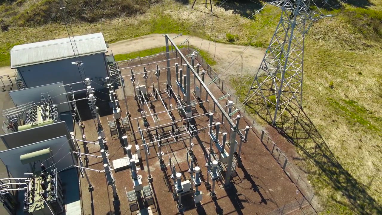 晴れた田園風景の中にある、変圧器、送電塔、配電線を備えた高電圧変電所。エネルギーインフラと送電網の空撮。