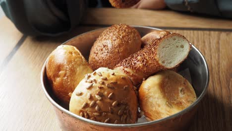 hand holding a piece of bread from a bowl of assorted breads on a wooden table