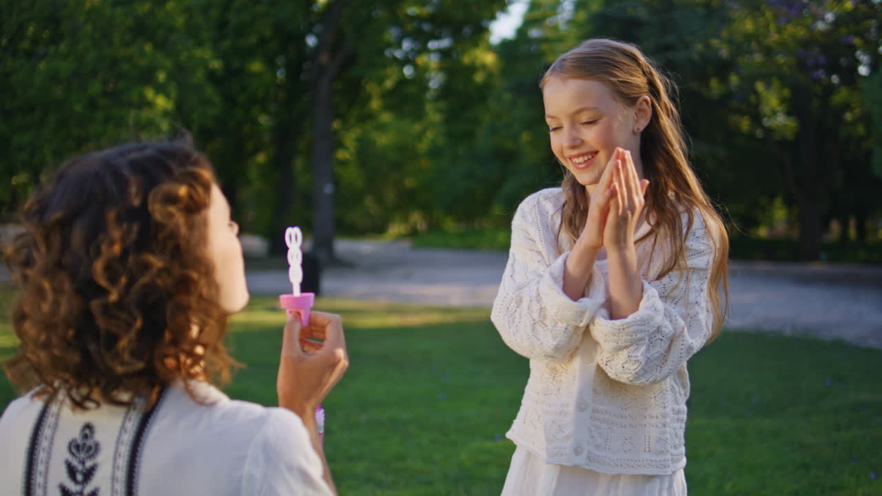 Mother daughter blowing soap bubbles on grass in sunshine park nature closeup