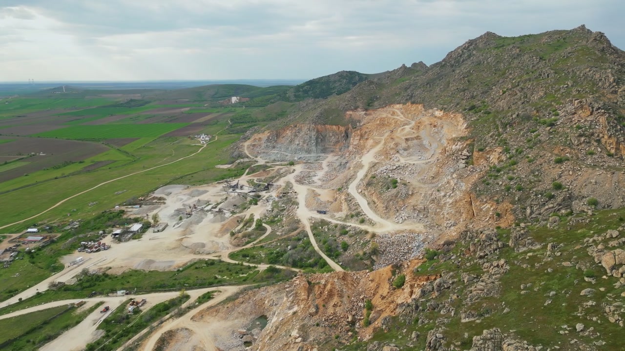 Rugged Granite Peaks Overlooking Rural Plains At Macin Mountains In The Dobrogea Region Of Tulcea County, Romania. Aerial Shot
