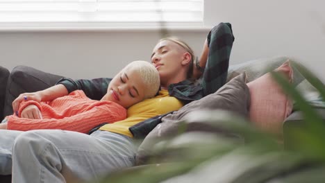 Happy-diverse-female-couple-embracing-and-lying-together-in-living-room