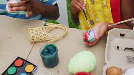 Animation-of-hands-of-diverse-grandmother-and-grandson-painting-easter-eggs-in-garden