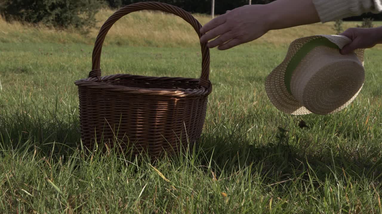 Ruce zvedající slaměný klobouk a pletený koš, střední záběr.