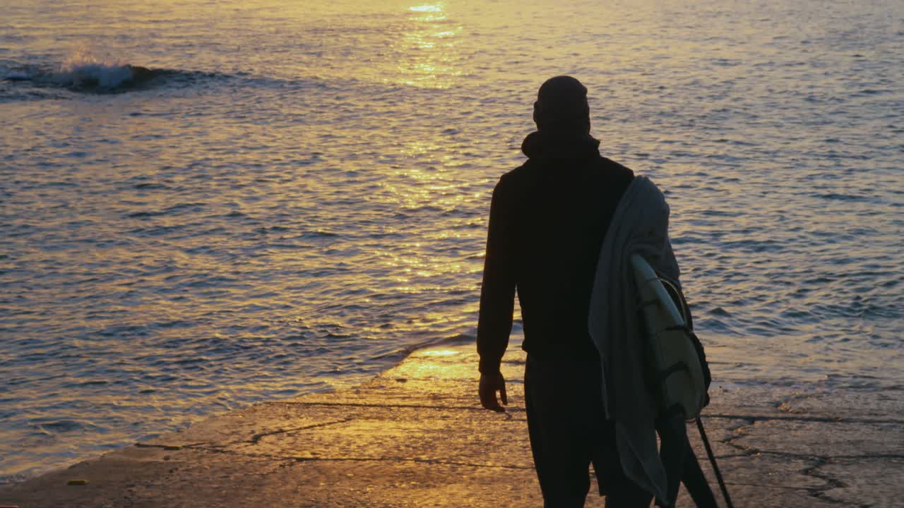 vista trasera de un hombre adulto con tabla de surf caminando por la playa 4k