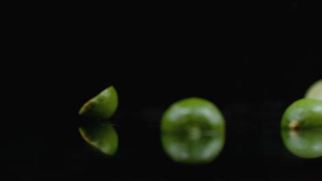 dos limas verdes maduras caen sobre el vidrio con salpicaduras de agua en cámara lenta sobre un fondo oscuro.