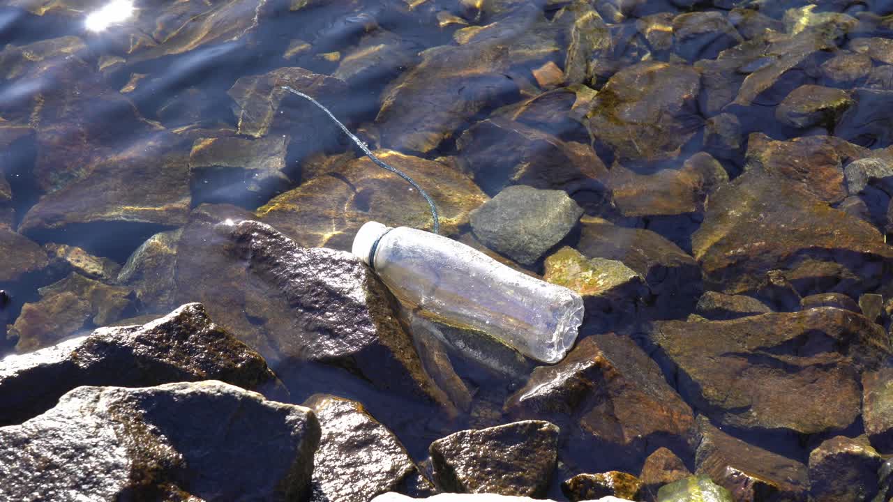 Muovipullo kelluu Norjan kivikkoisen vuonorannikon matalassa vedessä