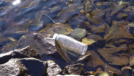 botella de plástico flotando en aguas poco profundas de la costa rocosa del fiordo noruego