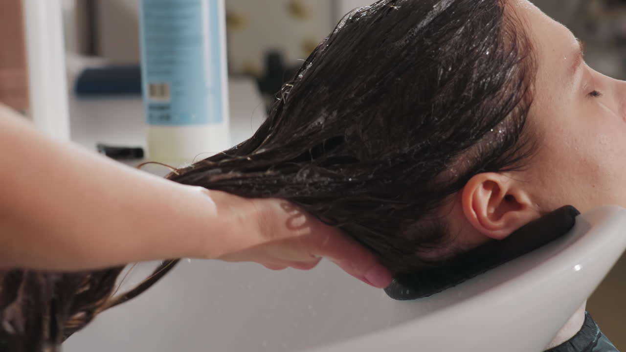 routine di pulizia dei capelli, primo piano del processo di applicazione dello shampoo e districamento con flusso d'acqua rilassante, vista dettagliata dello stylist che deterge e districa accuratamente i capelli con mani delicate e acqua lenitiva