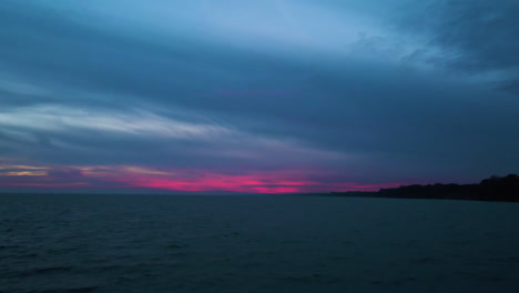 pink glow of dusk on horizon below ominous grey blue clouds at the coast