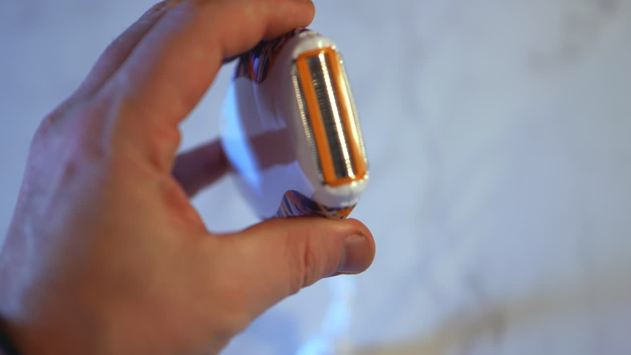 pequeña maquinilla de afeitar eléctrica de mano que obtiene la tapa superior de plástico volteada y vuelta a la cámara por mano blanca caucásica