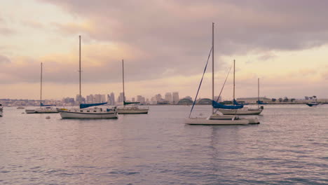 sailboats on water in san diego california harbor during pink cloudy sunset, coronado island with navy buildings and downtown in the background