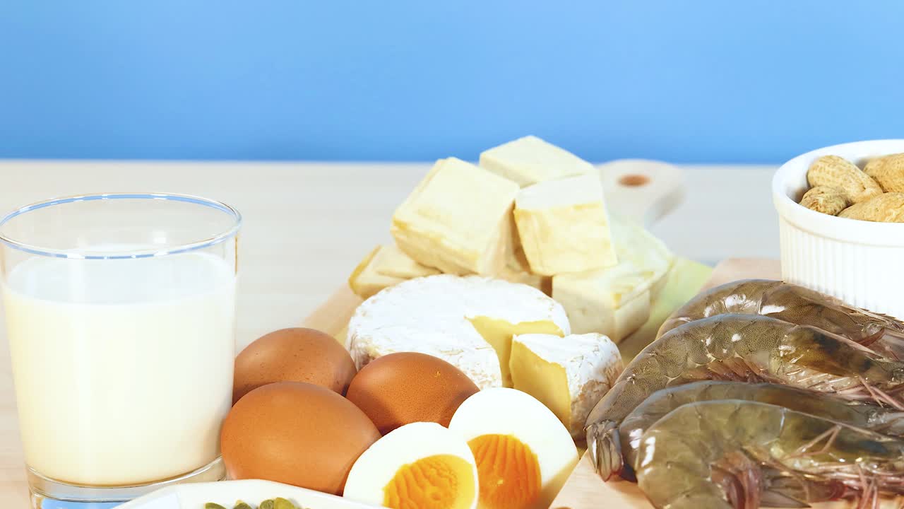 A vibrant display of various protein-rich foods including nuts, dairy, eggs, and seafood, set against a bright background