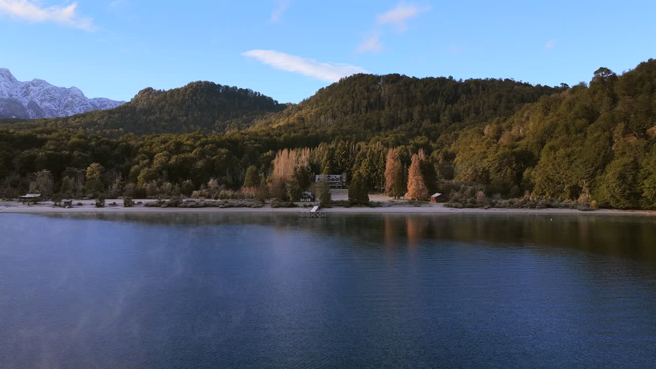 Spokojna woda jeziora Lago Espejo i piaszczysta plaża u podnóża zalesionych wzgórz w Parku Narodowym Nahuel Huapi, w pobliżu Villa La Angostura, Neuquén, Patagonia, Argentyna, w ekosystemie Andów Północnopatagońskich, ujęcie panoramiczne.