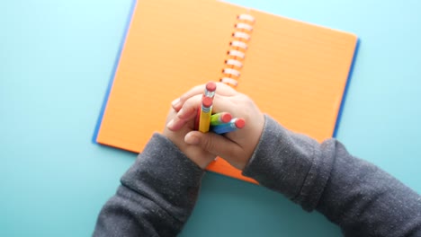 niño sosteniendo lápices de color sobre un cuaderno abierto
