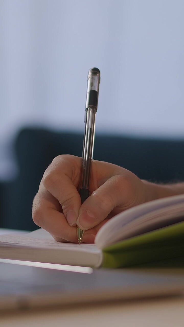 Close-up of a Hand Writing in a Notebook with a Pen