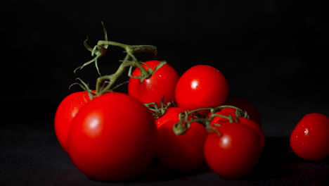 close up de un tomate cayendo en una pila de tomates en cámara lenta con un fondo negro