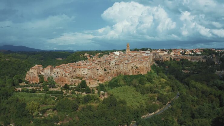 Drone footage of the historic medieval town Pitigliano, a masterpiece of ancient architecture on a rock in the idyllic landscape of Tuscany, Italy with green trees, blue hills and thunder storm clouds