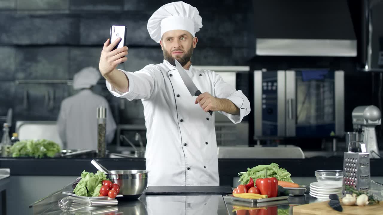 chef tomando una foto en la cocina. chef con un cuchillo tomando una selfie en el teléfono móvil.