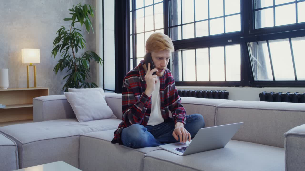 Man Talking on Phone and Working on Laptop at Home