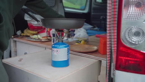 man cooks on a portable camping stove gas in a campervan near the mountains of donnamannen, norway