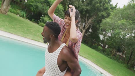 Happy-diverse-couple-at-swimming-pool,-man-carrying-woman-in-garden