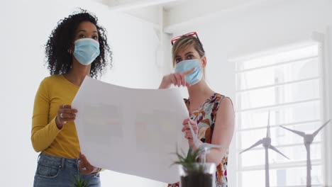 two woman wearing face mask discussing over document at office