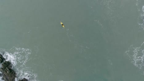 Von-Oben-Nach-Unten-Zeigt-Eine-Person,-Die-Mit-Einem-Gelben-Kajak-Zwischen-Zwei-Felsigen-Bereichen-Rudert,-Die-Für-Unruhiges-Wasser-Sorgen