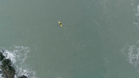 de arriba hacia abajo de una persona remando un kayak amarillo entre dos áreas rocosas que están creando aguas agitadas