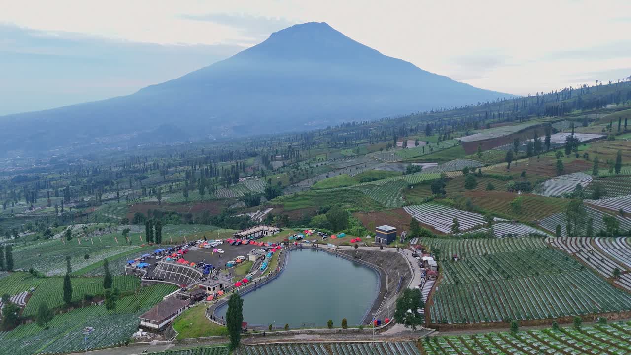 Aerial tropical rural landscape with scenery of water reservoir in the middle of plantation and view mountain on the background, Indonesia.