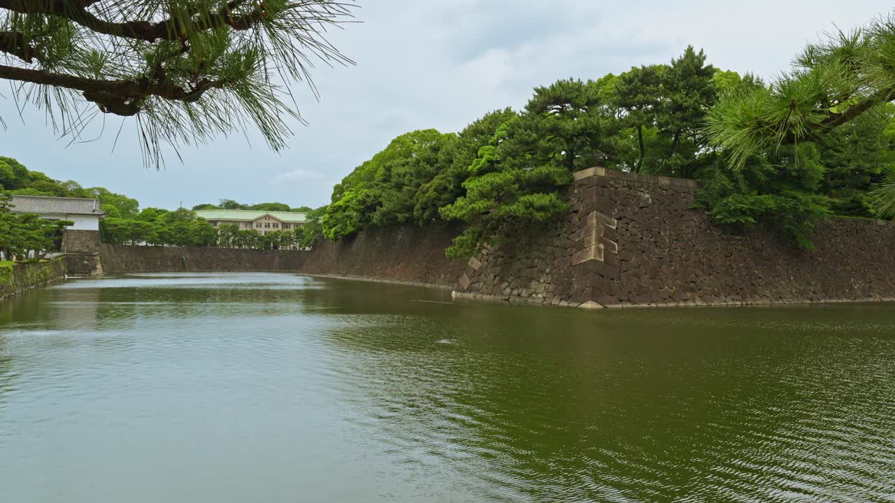 A tranquil view of the Edo Castle outer moat in Tokyo, showcasing its calm waters and the historic stone walls reflecting in the water.