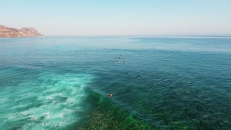 Aerial-drone-view-of-a-surfers-in-clear-waters-of-Sumbawa,-sunny-evening,-in-Asia