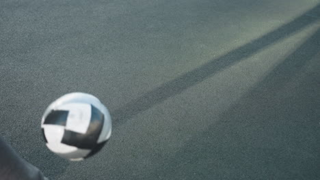 footballer in hoodie skillfully kicks soccer ball upward on urban sports field, capturing dynamic movement and intense focus. background includes residential buildings and goalpost