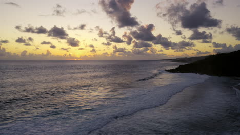 panorámica aérea a la izquierda de una hermosa puesta de sol en el océano mientras las olas rompen en una playa