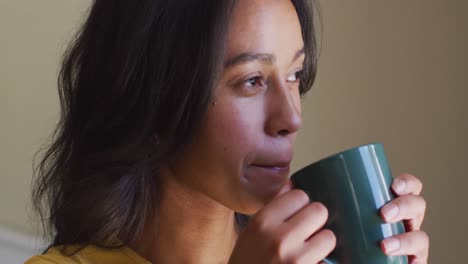 Profile-of-relaxed-biracial-woman-drinking-coffee-and-looking-outside-window