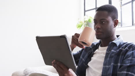relaxing at home, man sipping coffee while reading on tablet