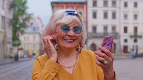 Senior-grandmother-woman-tourist-with-smartphone,-smiling,-listening-music-in-app-wearing-earphones