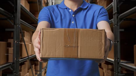 close up of a male courier in blue uniform showing a carton to camera while delivering it in warehouse