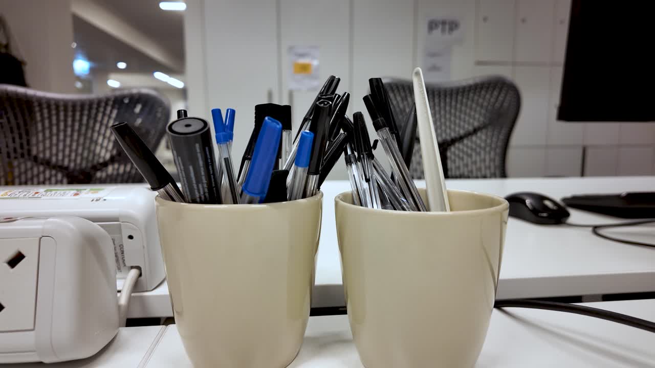 Office desk showing pens and stationery in mugs, ready for work
