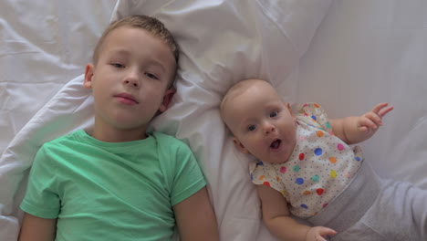 a brother and a baby sister lying on a bed close to each other