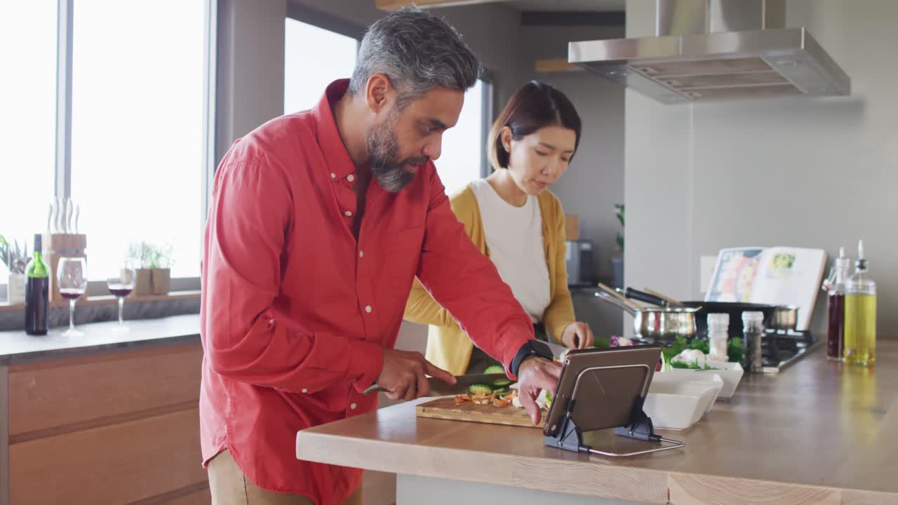 pareja feliz cocinando juntos, cortando verduras y usando tableta en la cocina