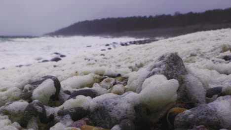 노르웨이의 arendal에 있는 skagerrak 해안에서 강한 파도가 던진 바위가 있는 해변에 남겨진 더러운 노란색 거품이나 거품.