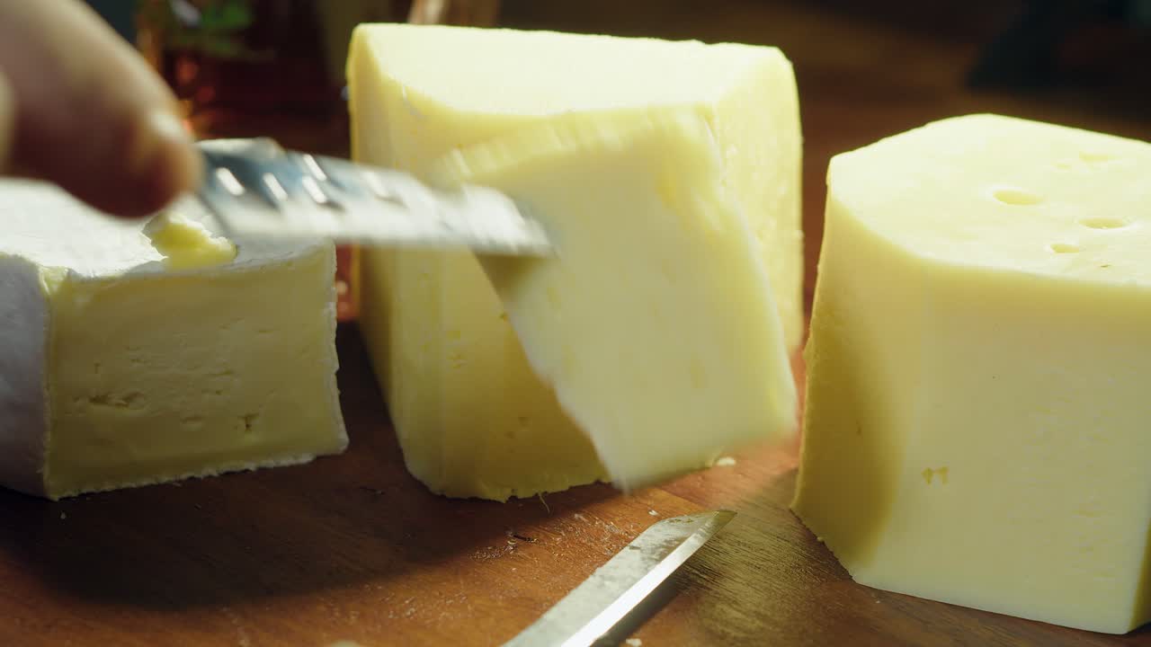 gouda, brie y queso suizo en tabla de cortar cortados con un cuchillo pequeño